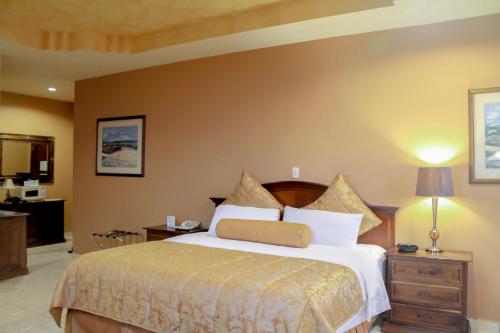 a bedroom with a bed and a dresser with a lamp at Hotel Monteolivos in San Pedro Sula