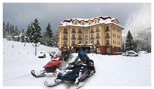 two people on a snowmobile in front of a building at Grand Hotel Pylypets in Pilipets