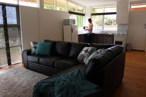 a living room with a black couch and a woman in the kitchen at My Port Lincoln Place in Port Lincoln