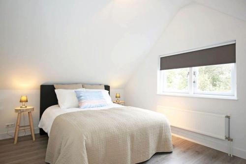 a white bedroom with a bed and a window at Salt Life Beachhouse in Noordwijk aan Zee