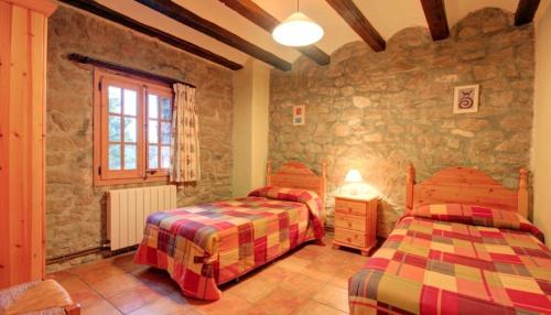 a bedroom with two beds and a stone wall at Mas Del Cigarrer Allotjament Rural in Horta de San Joan