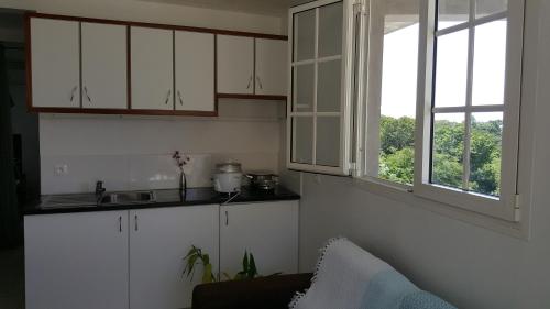 cocina con armarios blancos, fregadero y ventana en Studio Pleine Nature en Les Abymes