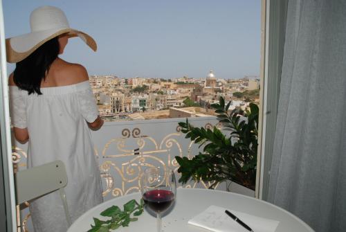 a woman in a white dress and hat looking out a window at Casa Cara in Birgu