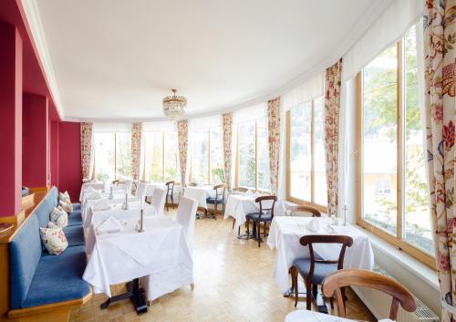 a restaurant with white tables and chairs and windows at Villa Excelsior Hotel & Kurhaus in Bad Gastein