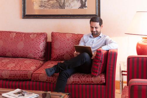 a man sitting on a couch with a tablet at Mercure Luxembourg Kikuoka Golf & Spa in Canach