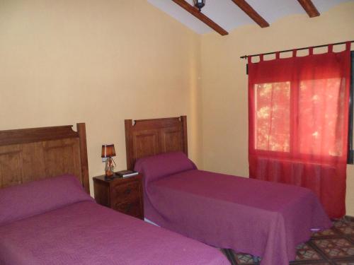 two beds in a bedroom with purple sheets and a window at Casa la Peña in Alpera