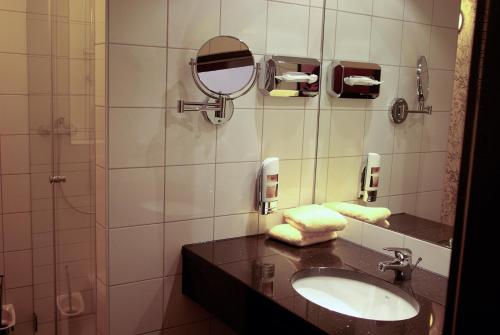 ein Bad mit einem Waschbecken, einem Spiegel und einer Dusche in der Unterkunft Hotel Sittardsberg in Duisburg