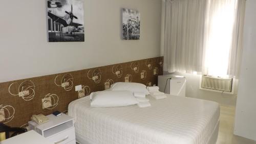 een slaapkamer met een bed met witte lakens en kussens bij Rede Andrade San Martin in Curitiba