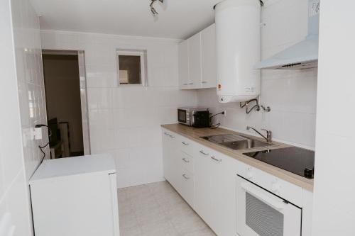 uma cozinha branca com armários brancos e um lavatório em A Casa do Jardim à Estrela I em Lisboa