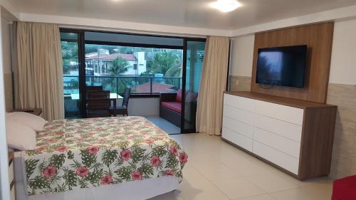 a bedroom with a bed and a television and a balcony at Praia Tabatinga AP Beira Mar com vista deslumbrante da praia in Jacumã