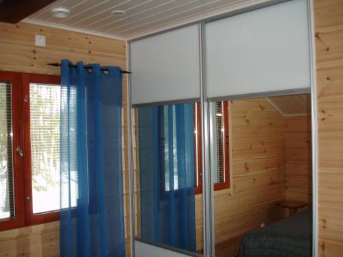 a bedroom with blue curtains in a wooden room at Aamuruskon Ukkola Cottage in Sirkkakoski