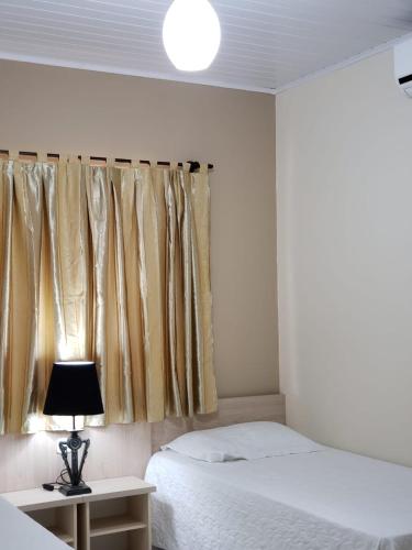a bedroom with a bed and a lamp and a window at Felipe Family Houses - Casas de temporada in Foz do Iguaçu
