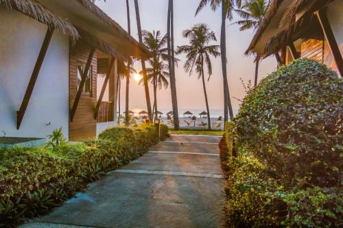 a walkway next to a house with palm trees at Eskala Hotels and Resorts in Ngwesaung
