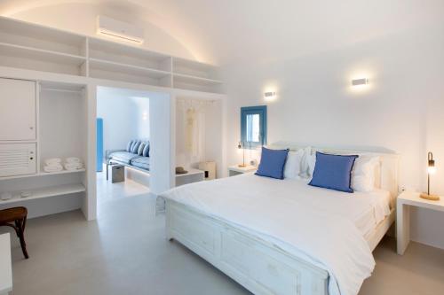 a white bedroom with a large bed with blue pillows at Akrotiri Cove in Akrotiri