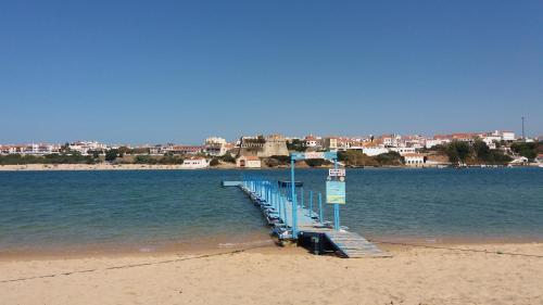 a dock on a beach with a city in the background at Apartamento Estúdio Pinhalmar in Vila Nova de Milfontes