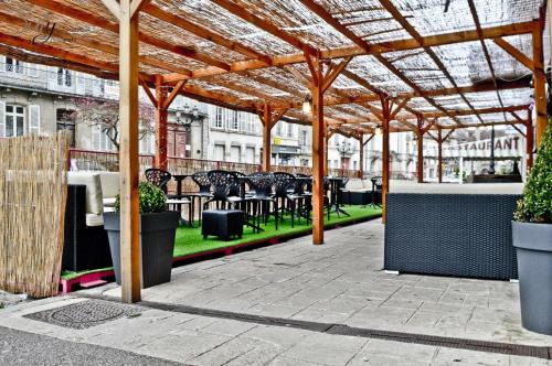 een patio met tafels en stoelen onder een houten pergola bij Hôtel du Commerce in Semur-en-Auxois