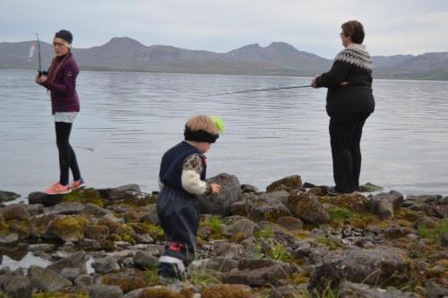 two adults and a child fishing on the rocks by the water at Thingvellir Lake Cottage in Veiðilundur