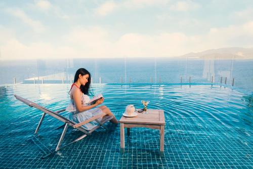 a woman sitting on a chair next to a swimming pool at V Hotel Nha Trang in Nha Trang