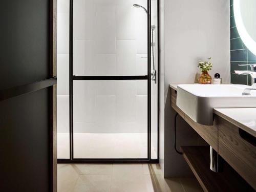 uma casa de banho com uma cabina de duche em vidro e um lavatório. em Novotel Sydney Darling Square em Sydney