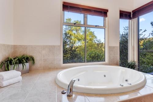 a large white tub in a bathroom with windows at Ravensbourne Escape- Kookaburra Kottage in Ravensbourne