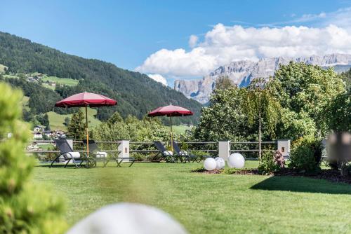 a lawn with chairs and umbrellas with mountains in the background at Rainell Dolomites Retreat in Ortisei