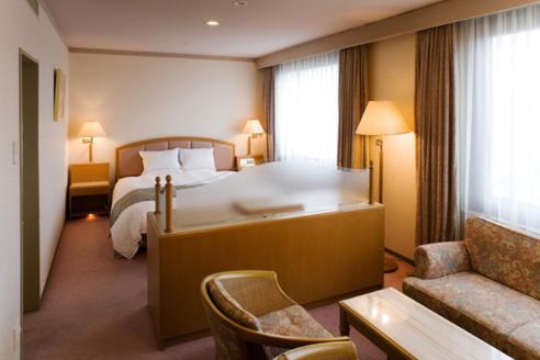 een hotelkamer met een groot bed en een bank bij Hotel Higashinihon Utsunomiya in Utsunomiya