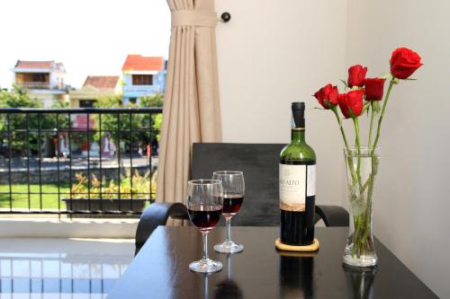 a bottle of wine and two glasses of red roses on a table at Hoi An Green View Homestay & Villa in Hoi An