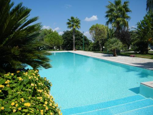 a swimming pool with blue water and palm trees at Agriturismo Torrevecchia in San Pancrazio Salentino
