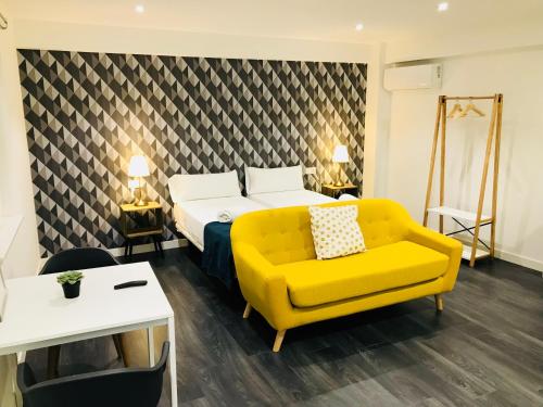 Habitación de hotel con cama y sofá amarillo en Apartamentos Arriba by gaiarooms, en Salamanca