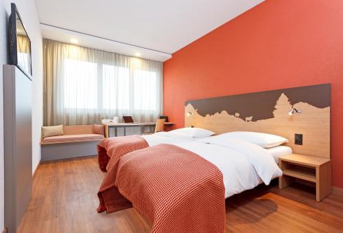 a bedroom with two beds and an orange wall at SwissEver Zug Swiss Quality Hotel in Zug