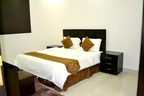 una camera da letto con un grande letto con lenzuola bianche e cuscini dorati di الخربوش للشقق المخدومة a Hafr Al Baten