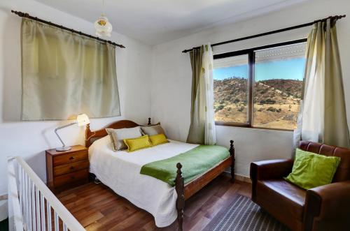 a bedroom with a bed and a chair and a window at Mértola low-cost in Mértola