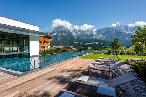 a house with a swimming pool with mountains in the background at Hotel Der Bär in Ellmau