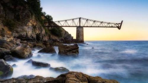 a bridge over the water next to the ocean at Castro Sun And Beach in Castro-Urdiales