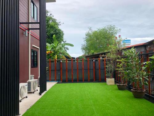 a yard with green grass and a red fence at Thyme Xeriscape Hostel in Kanchanaburi