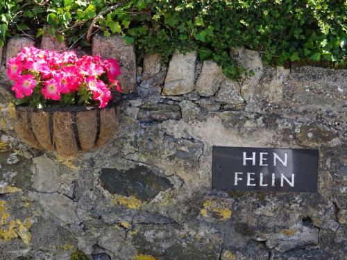 a sign on a stone wall with pink flowers at Yr Hen Felin - The Old Mill B&B in Morfa Nefyn