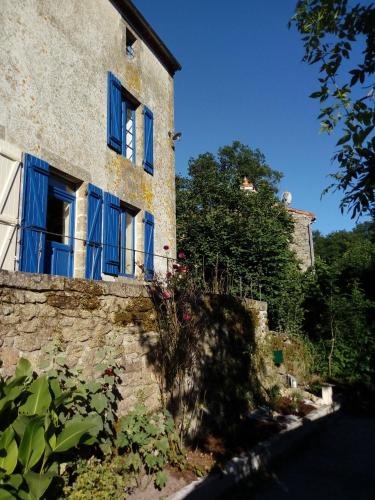 Cette maison ancienne est dotée de fenêtres bleues et d'un mur en pierre. dans l'établissement Gîte les Pieds dans l'eau 10 min du Puy du Fo, à Treize-Vents