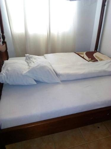 a pair of beds with white sheets on them at Rena Akasha Establishments in Kyenjojo