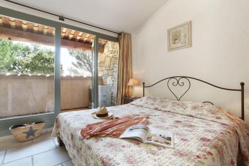 1 dormitorio con cama con libro y ventana en Résidence Prestige Odalys La Bastide des Chênes, en Gordes