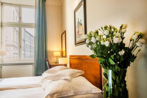 un jarrón lleno de flores blancas sentado junto a una cama en Hotel Senacki, en Cracovia