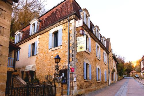 un bâtiment en briques avec une horloge dans une rue dans l'établissement Hôtel Pontet, à Beynac-et-Cazenac