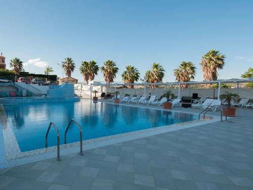 a swimming pool with chairs and palm trees in the background at Grand Hotel Paradiso in Catanzaro Lido