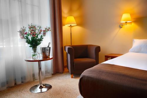 a hotel room with a bed and a chair and flowers at Focus Hotel Łódź in Łódź