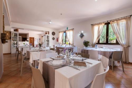 a restaurant with white tables and chairs and windows at Hotel Achibea in San Vito lo Capo