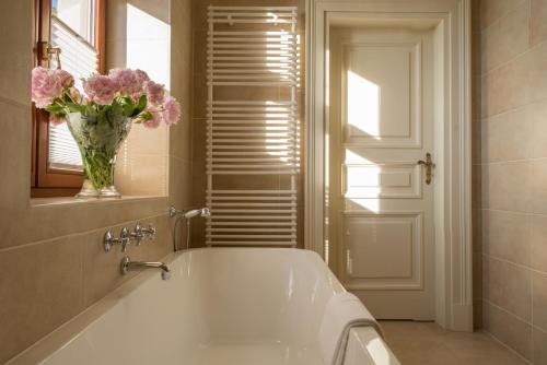 a bathroom with a tub with a vase of pink flowers at Pałac Warlity in Olsztynek