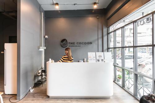a woman sitting at a counter in a store at The Cocoon Hostel in Bangkok