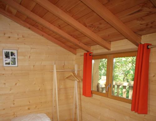 Habitación con paredes de madera y una ventana con cortinas rojas. en Nuits perchées à Laroque, en Saint-Antoine-de-Breuilh