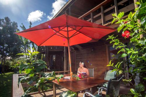 a woman sitting at a table under a red umbrella at Cabañas Tokerau in Hanga Roa