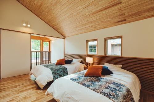 two beds in a room with wooden ceilings and windows at PICA Fujiyama in Fujikawaguchiko