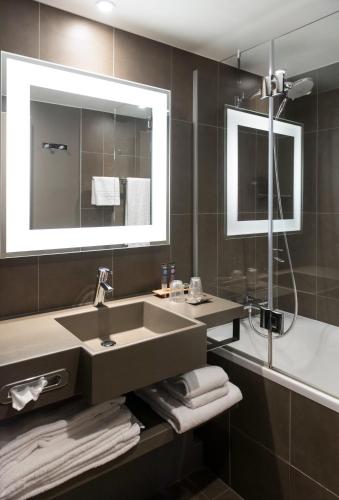 a bathroom with a sink and a tub and a mirror at Novotel Brussels Airport in Diegem